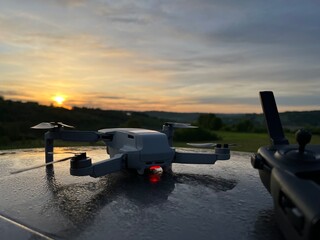Kontroler drona z wyświetlaczem i dron w tle w plenerze ze wschodem słońca © VILKTERIO