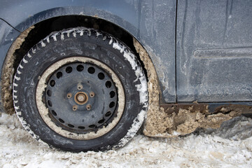  A car wheel covered in snow and mud, indicating it has been driven on wintry, dirty roads. The...