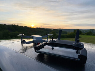 Kontroler drona z wyświetlaczem i dron w tle w plenerze ze wschodem słońca © VILKTERIO