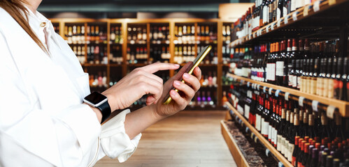 Businessperson using smartphone in liquor store. E-commerce and retail. Selling wine online....