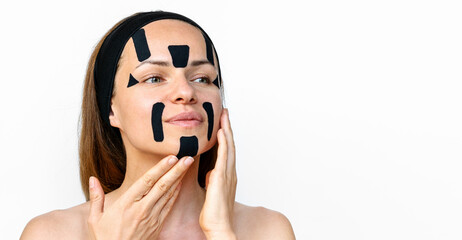 Female beauty model applying kinesio facial tapes on her face against a white background in...