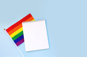 Blank mock up notebook on rainbow LGBTQ flag, blue background. June proud pride month parade, gay...