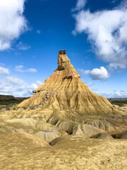 Las Bardenas Reales. Sentry of the Plains. Desert. A towering, cone-shaped rock formation stands under a cloudy sky, surrounded by flat terrain.
