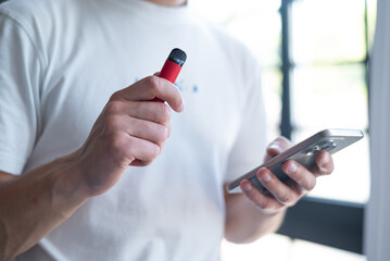 red disposable electronic cigarette with phone in a man's hand. Modern online communication	