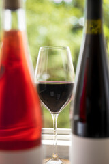 Glass filled with dark red wine at the center, surrounded by bottles of wine on either side, product photography, in sunny day after harvest.