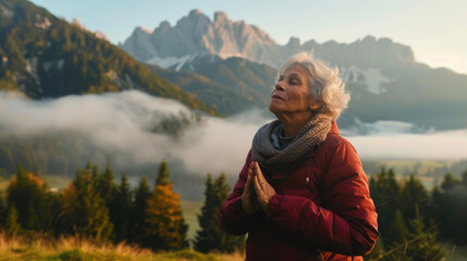 Elderly woman in the mountains does breathing practices in nature. A beautiful gray-haired woman practices meditation in nature in the early morning against the backdrop of fog. Nature concept.
