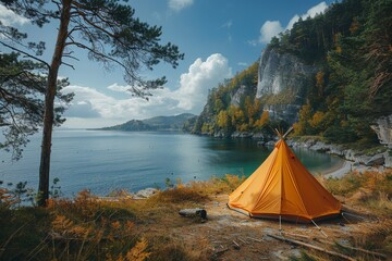 Obraz premium An isolated bright orange tent set up on a shore, overlooking a serene lake surrounded by autumnal forest and rocky cliffs