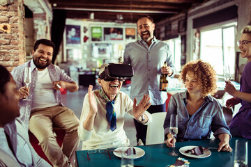 Diverse group of people laughing with senior woman using VR headset at office party