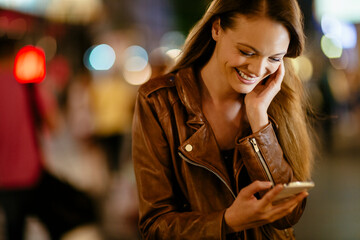 Young woman using smartphone downtown in the city at night