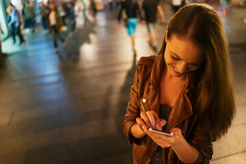 Young woman using smartphone downtown in the city at night