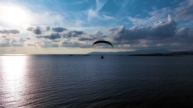 Close-up of a paramotor tricycle suspended under a parachute in the air. Drone shooting of man with paramotor flying in the air
