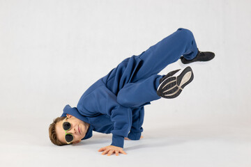 Boy in breakdancing position.Hip hop dance. Bboying basics. Boy in a blue tracksuit on a white background.Cheerful boy dancing breakdance