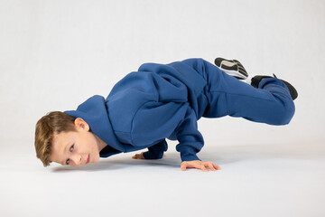 Boy in breakdancing position.Hip hop dance. Bboying basics. Boy in a blue tracksuit on a white background.Cheerful boy dancing breakdance
