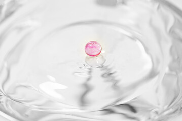 Splash in a glass, drop of violet liquid falling into a transparent glass, light background, selective focus