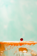 Splash in a glass, drop of orange liquid falling into a transparent glass, light background,...