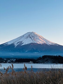 A majestic snow-capped fuji mountain rises majestically above a tranquil lake, its peak piercing the clear blue sky.