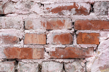 Textured old brick wall background. Close-up view of weathered pink paint over red brick wall surface covered with spots and streaks. Copy space for your text and decorations. Abstract backdrop theme.