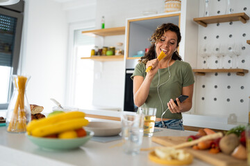 Young woman listening music on the headphones and singing while making pasta for lunch.