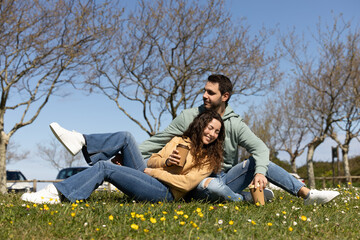 happy couple resting on the grass with thermoses of coffee golding in their hands
