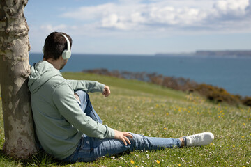 guy sitting on the grass listening to music looking to the sea