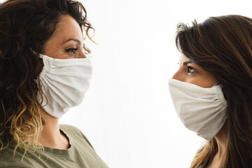 Portrait of two adult women looking at each other with empathy wearing protective face masks.