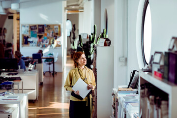 Senior female fashion designer holding documents in modern design studio workspace