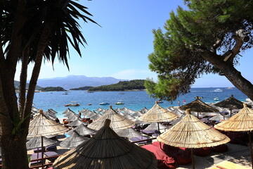 Ksamil beach with sunbeds and straw umbrellas on the Albanian Riviera, with the blue sea and island of Corfu in the background. Vacation concept.