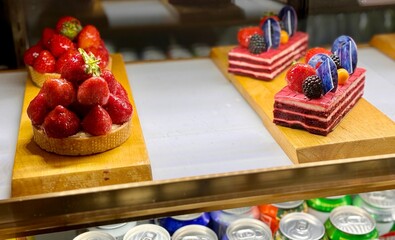 A portion of layered cream cake with red strawberries on a wooden stand on the counter of the restaurant. Close-up