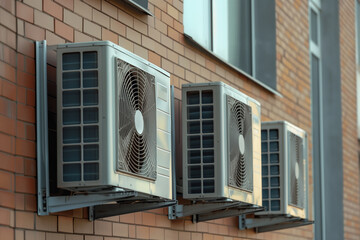Air Conditioning Units on Building Exterior. Three air conditioning units mounted on the side of a modern building, featuring visible fans and grills.