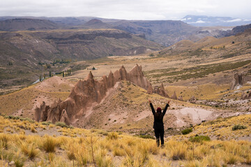 Tourist raising his arms in happiness in a desert landscape with giant rocks and grasslands in a...