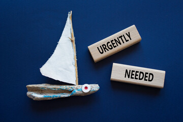 Urgently needed symbol. Concept word Urgently needed on wooden blocks. Beautiful deep blue...