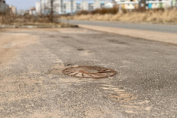 A rusty iron hatch with a pattern above an observation well is located on auto road in daytime. Close-up