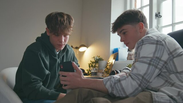 Close up shot of two teenage boys laughing and having fun looking at social media post or streaming online on mobile phone in bedroom at home - shot in slow motion