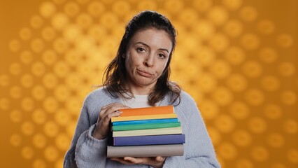 Portrait of woman with pouting expression holding pile of books, showing disproval of reading...
