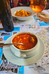 A delicious soup served in a white bowl, placed on a travel-themed placemat. The placemat showcases various tourist destinations, suggesting a combination of culinary and tourism.