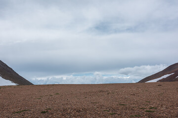 Minimalist layered landscape with high alpine pass and low cloudy sky in changeable weather....