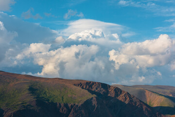 Huge dramatic lenticular cloud on white lush cloudy hill in blue sky. Beautiful cloudscape with big...