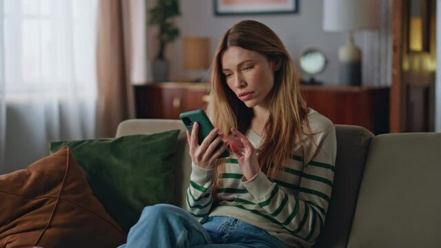 Stressed girl looking cellphone screen reading bad news at couch. Upset woman