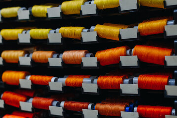 amount of different skeins of threads on special shelves in sewing studio or atelier, several colours, yellow and orange, handmade and sewing concept