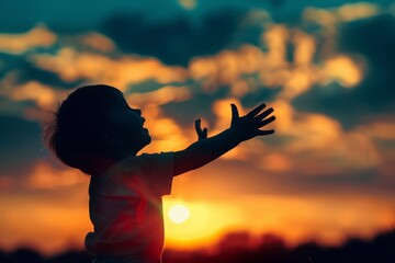 Little girl enjoying the sunset. Silhouette of a happy child at sunset. The girl raised her hands up and rejoices. The concept of happiness, carelessness, and enjoying the moment.