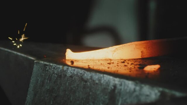 Person hitting hot smelted metal and causing flying sparks over an anvil
