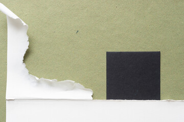 torn piece of paper and black paper tile on rough green paper with space