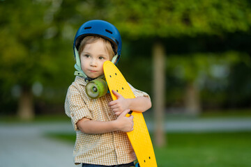Cute little boy learning to skateboard on beautiful summer day in a park. Child wearing safety helmet enjoying skateboarding ride outdoors.