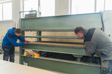 two craftsmen sliding a wide wooden panel in the belt grinder machine. High quality photo