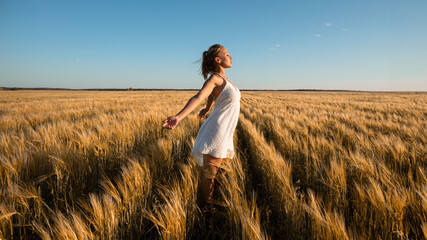 A happy woman in white dress standing in wheat field under blue sky
