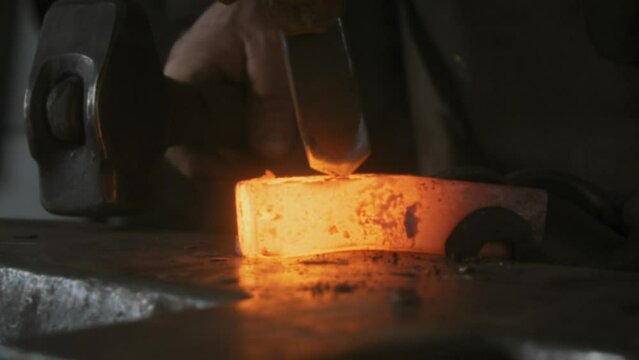 Blacksmith striking hot glowing metal with a chisel and hammer