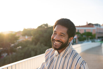 Young smiling black man walking on the pedestrian bridge above the city at the sunset