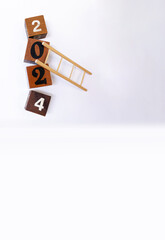 Año 2024. Espacio para copiar texto, mensaje, reflexión, resultado o balance. Cubos y escalera de madera. Plano vertical y fondo blanco. 