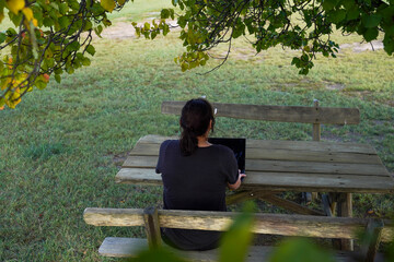 Fototapeta premium Woman working remotely on a wooden bench under a tree