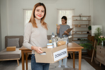 A beautiful female volunteer carries a donation box with canned food and food to donate to the...
